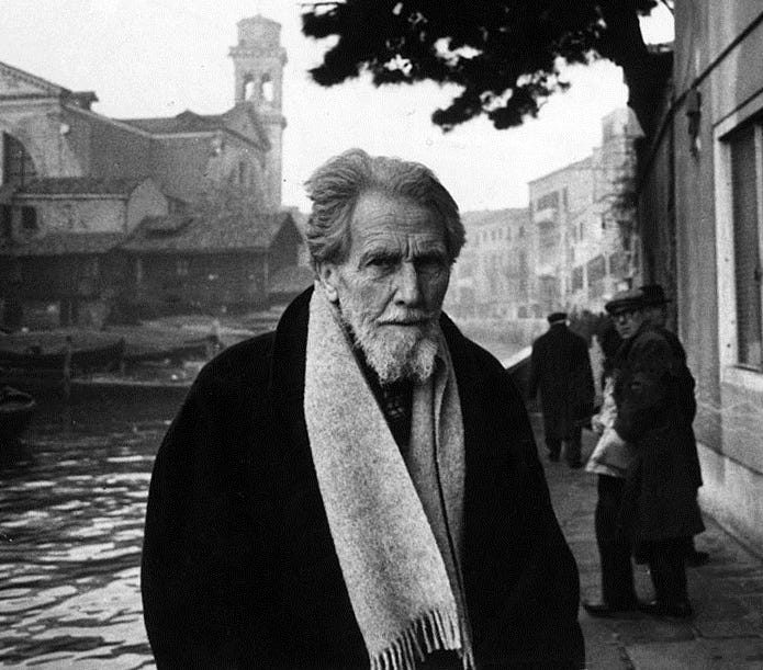Pound in Venice against backdrop of canal in dark coat with light scarf and piercing stare; pedestrians in background turning to stare at the camera
