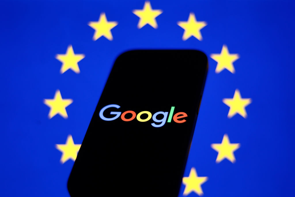 European Union flag displayed on a laptop screen and Google logo displayed on a phone in front of it European Union flag displayed on a laptop screen and Google logo displayed on a phone in front of it