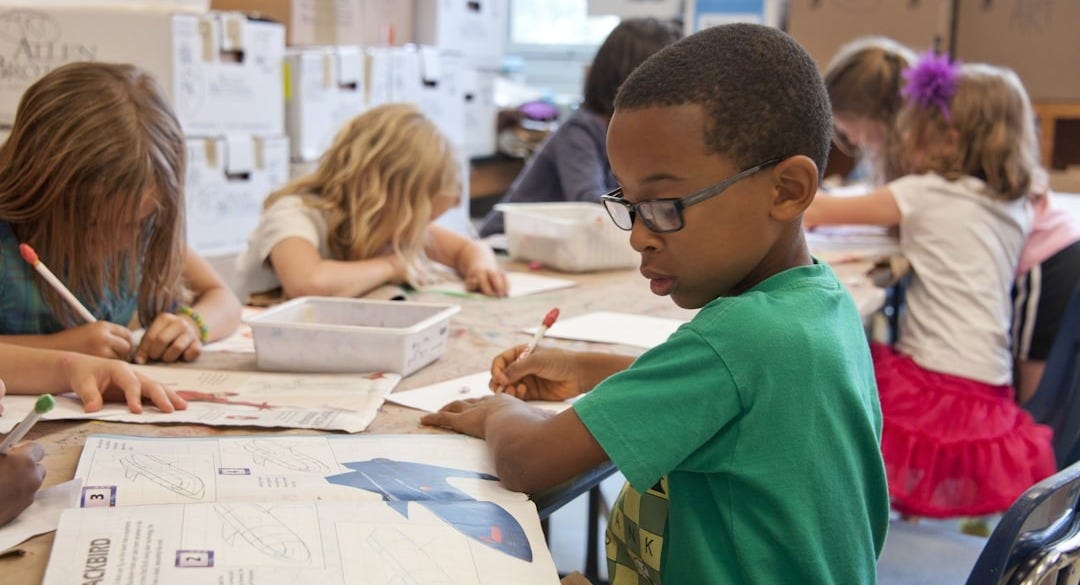 boy in green sweater writing on white paper