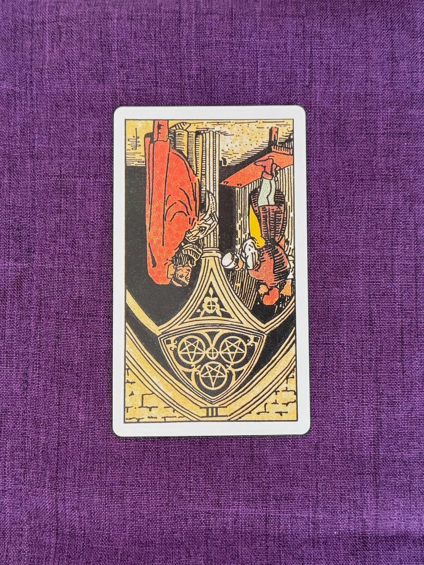 The Three of Pentacles shows a young stonemason working with his tools on a portion of a cathedral. In front of him two architects hold the plans for the design. The stonemason appears to be discussing his progress so far with the architects.