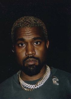 This may contain: a man with a beard wearing a gold chain and a green t - shirt is staring at the camera