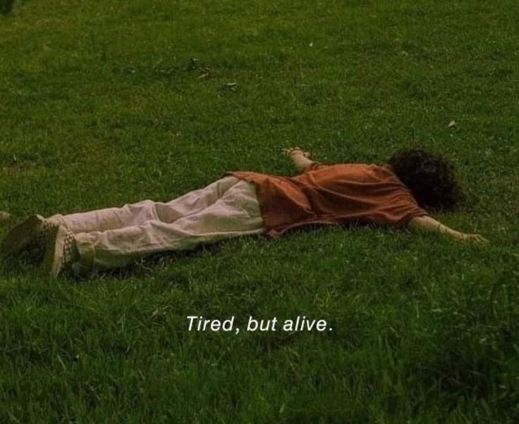 This may contain: a person laying in the grass with their head on his back and arms behind him that says tired, but alive