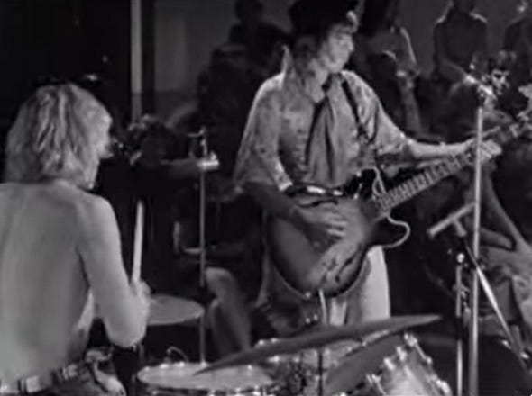 a black and white video still of a shirtless drummer and a bassist in paisley