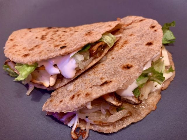Two folded tortillas stacked on a plate, with lettuce and crema dripping out Two folded tortillas stacked on a plate, with lettuce and crema dripping out