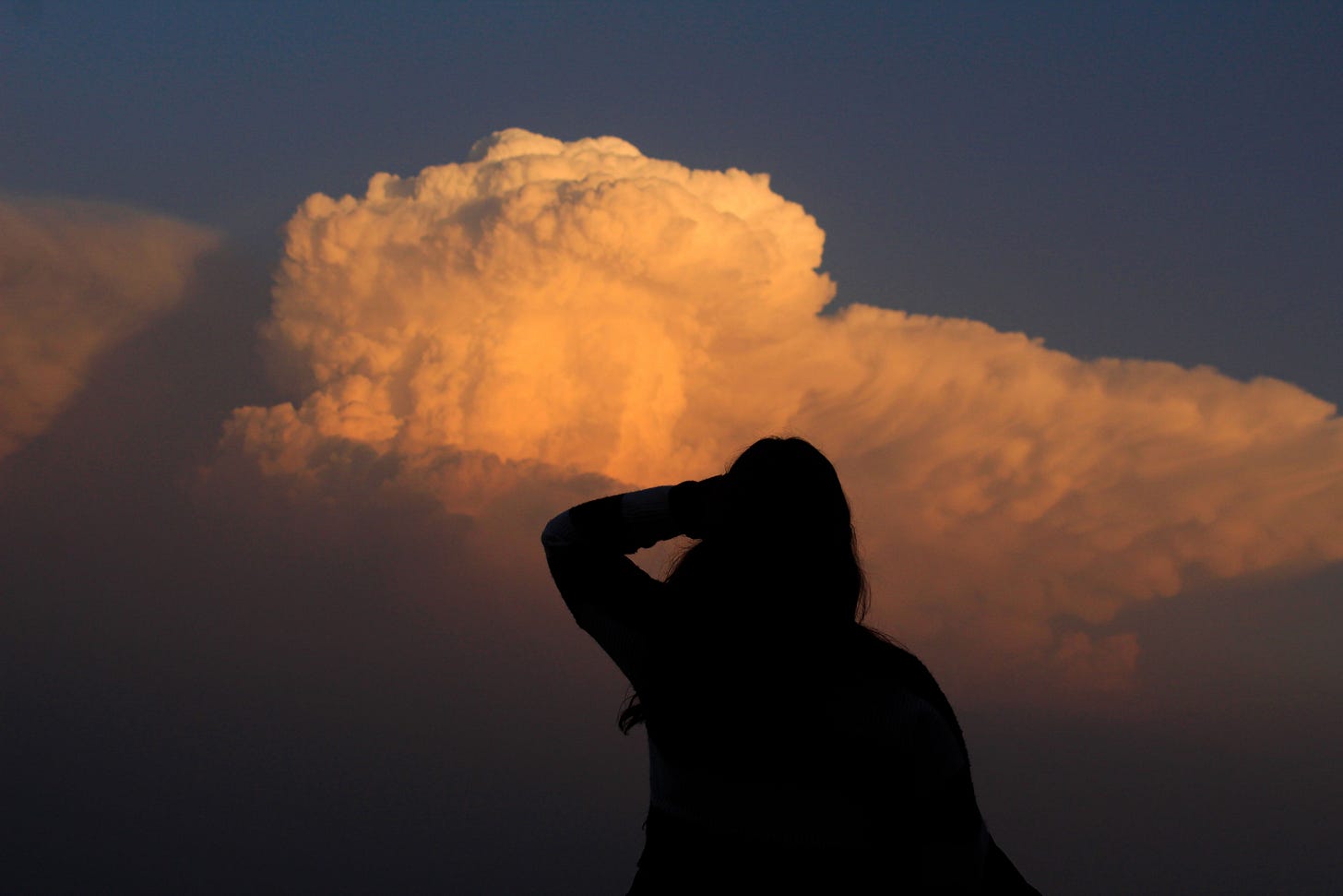 Schattenportrait einer langhaarigen Frau, die in den rötlichen Abendhimmel schaut