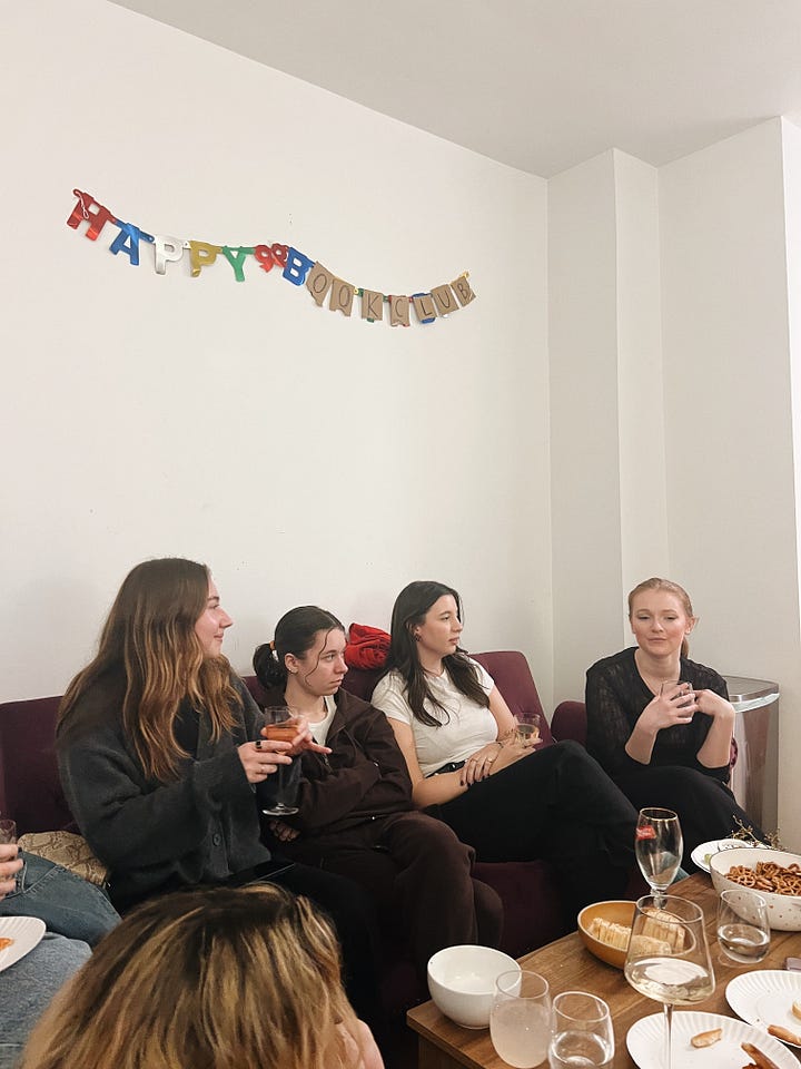 Girls sitting on couch for book club; girl opening wine bottle