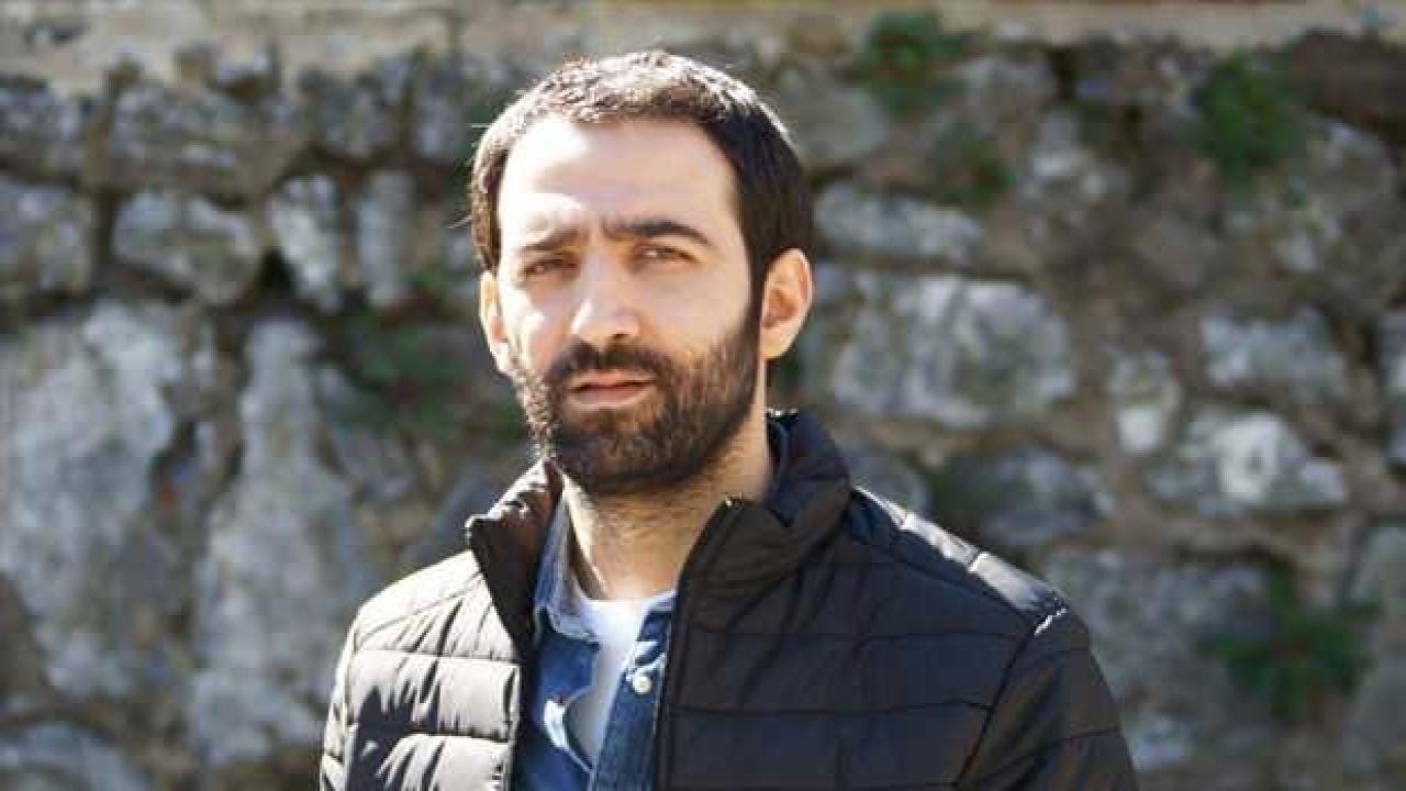 Ferit Kaya, siyah mont giymiş halde taş duvar önünde çekilmiş portre fotoğrafı. Bakışlarındaki derinlik ve karakteristik sakalıyla dikkat çekiyor, rol aldığı bir projeden tanıtım fotoğrafı olabilir.