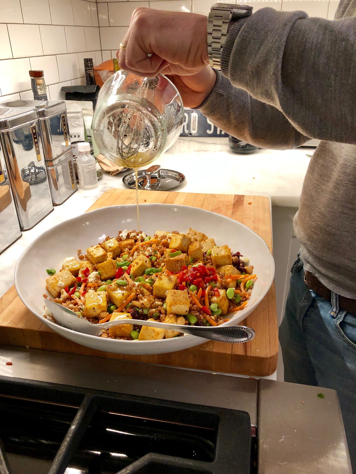 a hand reaches over a bowl of tofu and veggies pouring a dressing on top. 