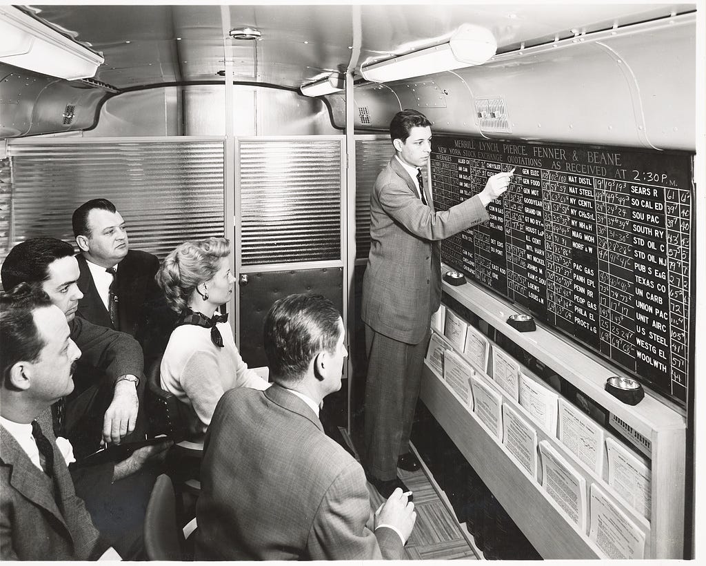 Black and white photo of executives at Merrill Lynch in the 1950s as stock prices are shown Black and white photo of executives at Merrill Lynch in the 1950s as stock prices are shown