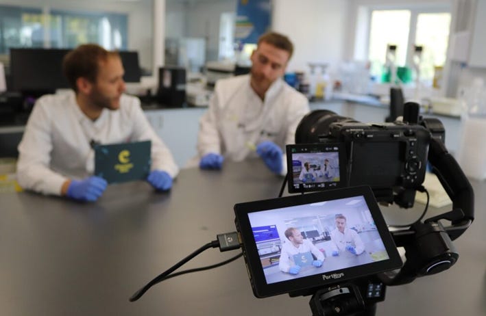Two people in lab coats talking whilst being filmed