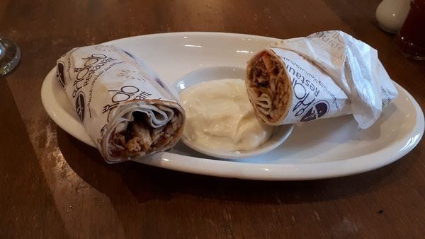 rolled up chicken schwarma with dip on a white plate