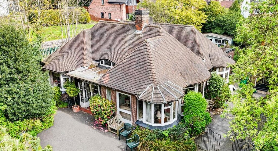 A brick bungalow with a brown tiled roof and green trees around it