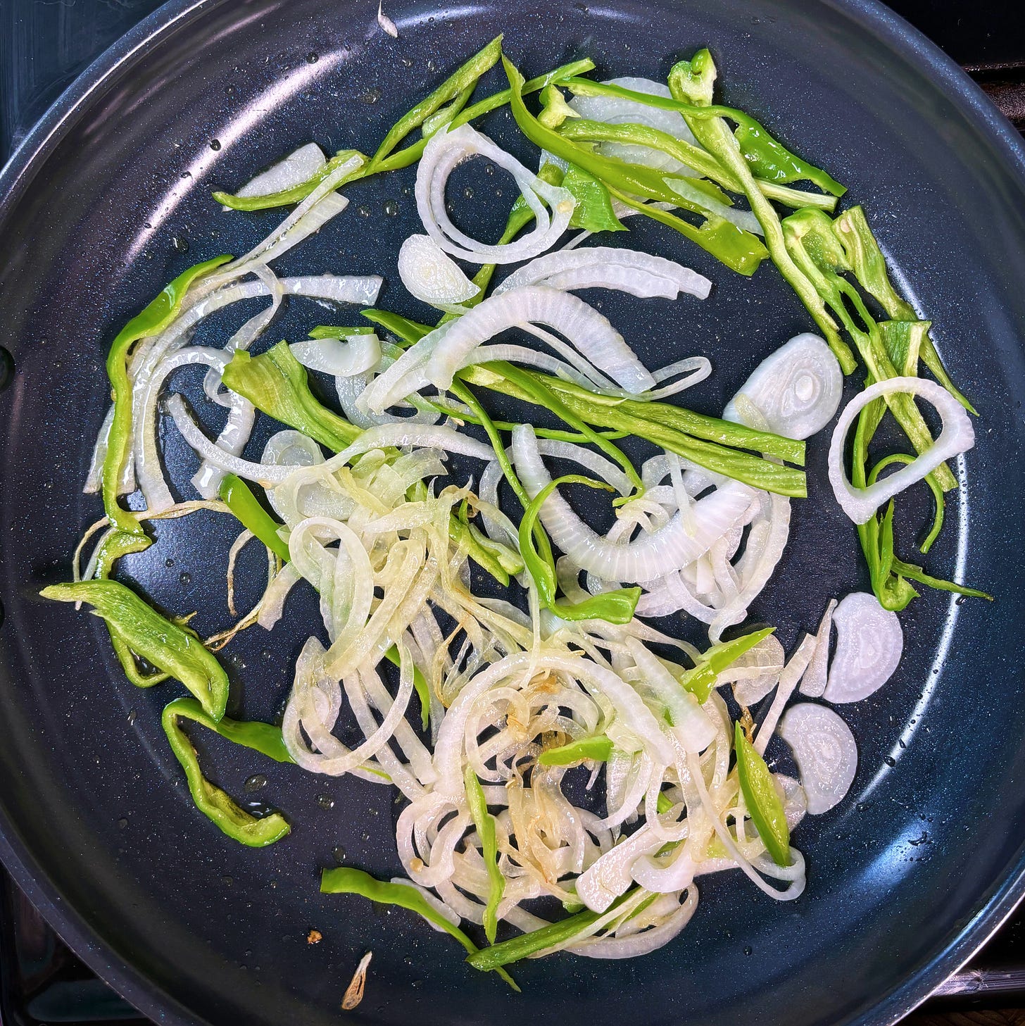 overhead view of sliced onions and green peppers in a blue saute pan overhead view of sliced onions and green peppers in a blue saute pan