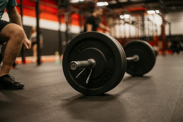 photograph of a barbell in a gym with a man sitting on the edge of the frame, taking a rest