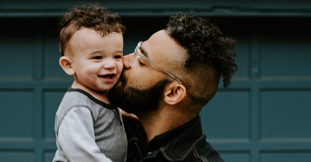 man carrying baby boy and kissing on cheek man carrying baby boy and kissing on cheek