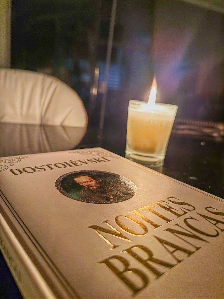 Livro "Noites Brancas", capa branca almofadada com foto do autor no centro, e ao lado do livro há uma vela acesa, o ambiente é escuro.