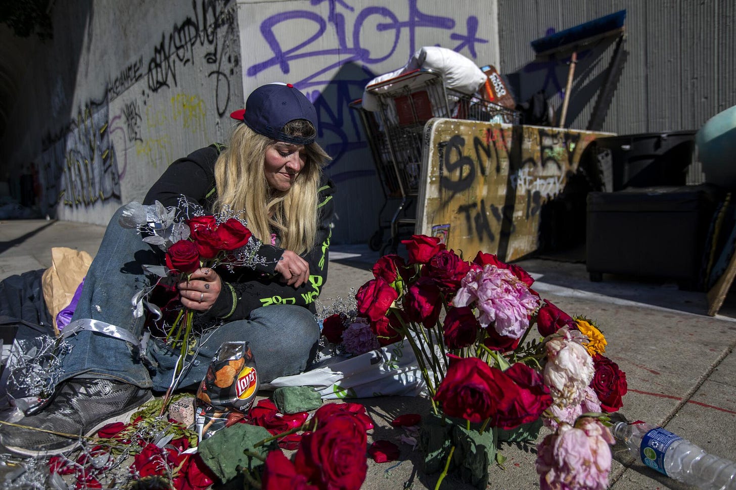 A woman sits while arranging flowers on a sidewalk. A woman sits while arranging flowers on a sidewalk.