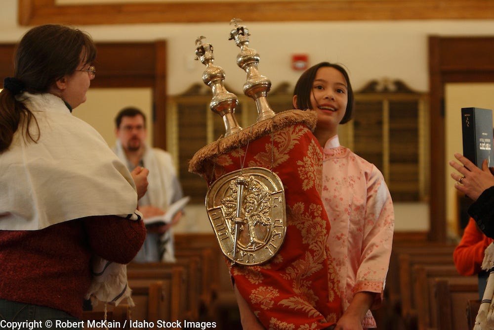 IDAHO. Boise. Asian Jewish girl carrying Torah for Hakifah in Ahavath Beth Israel synagogue while woman touches it with Tzitzit. MR | Idaho Stock Images IDAHO. Boise. Asian Jewish girl carrying Torah for Hakifah in Ahavath Beth Israel synagogue while woman touches it with Tzitzit. MR | Idaho Stock Images