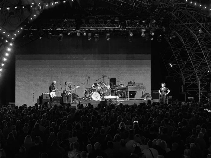 Deacon Blue are playing in front of crowded audience, Photo is black and white. Ricky is singing and lorraine is facing him with her hands on her hips