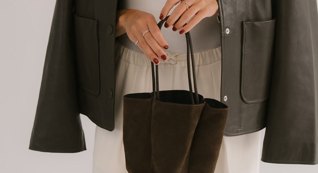 A close-up of a woman with red nails wearing a suede jacket and holding a suede bag A close-up of a woman with red nails wearing a suede jacket and holding a suede bag