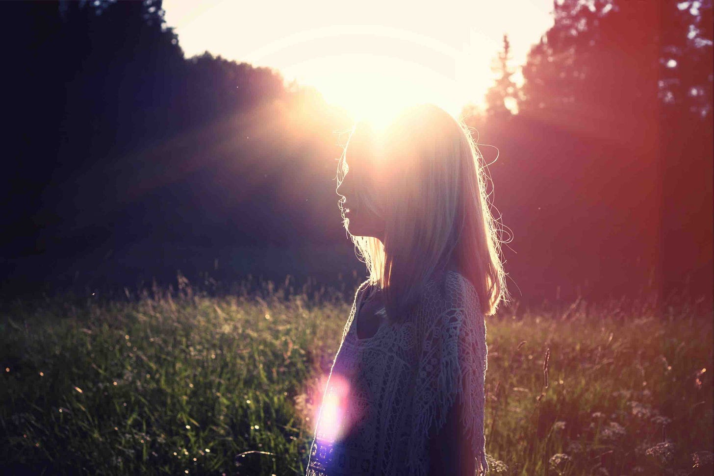 Woman in field with a setting sun reflecting behind her Woman in field with a setting sun reflecting behind her