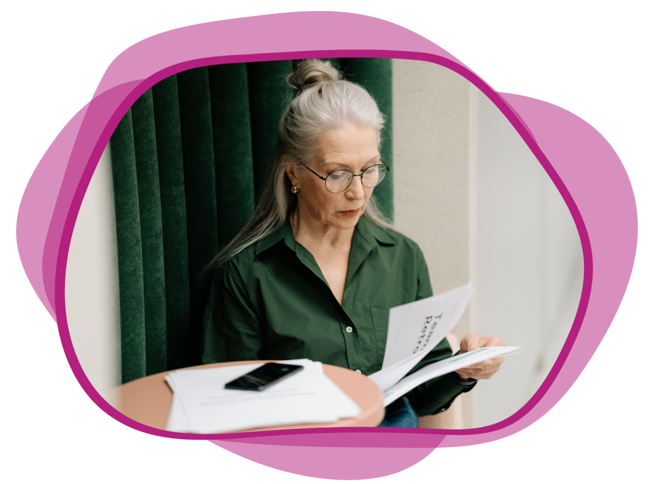 A woman reads through sheets of paper, standing next to a table with her phone and more sheets of paper on it.