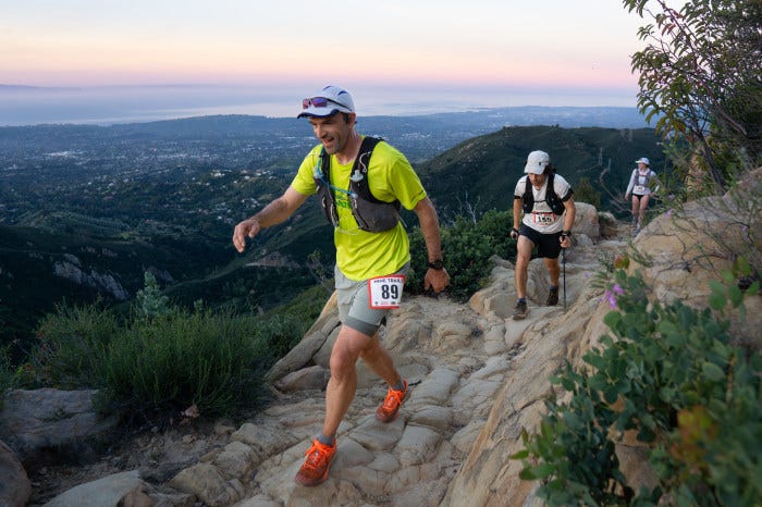 Tony Leach trail running with other runners on a rocky mountain path at dusk.