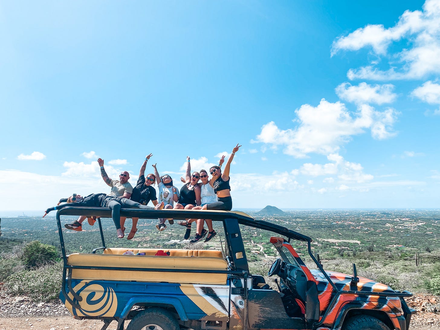 A group of people sitting on top of a Jeep with the island of Aruba in the background