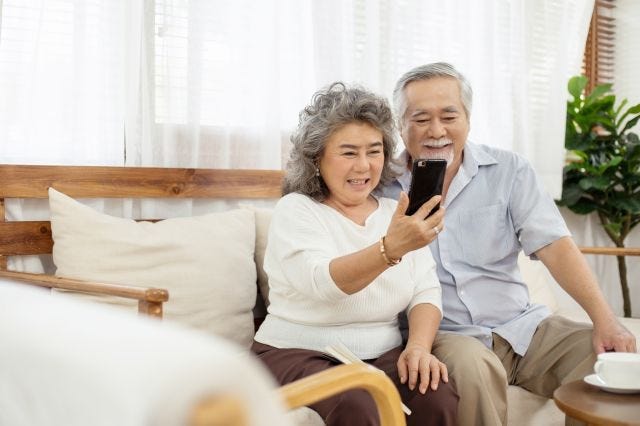 Happy couple sitting on sofa using smartphone video call