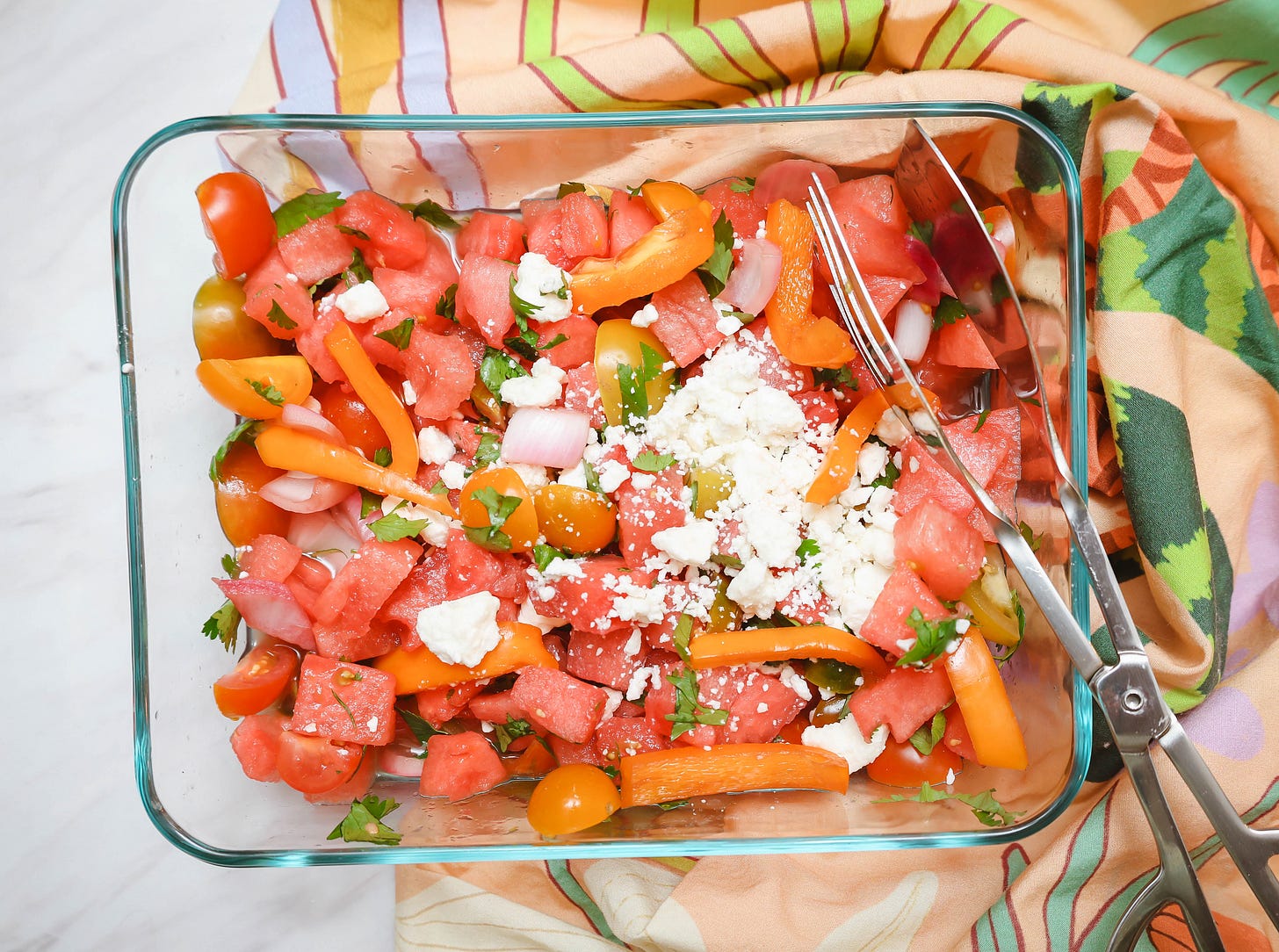 Heirloom tomato watermelon salad in a glass serving dish with sweet watermelon, cherry tomatoes, mini sweet peppers, pickled red onions, fresh herb cilantro, and crumbled feta, a colorful Southern summer side dish for cookouts and Juneteenth gatherings
