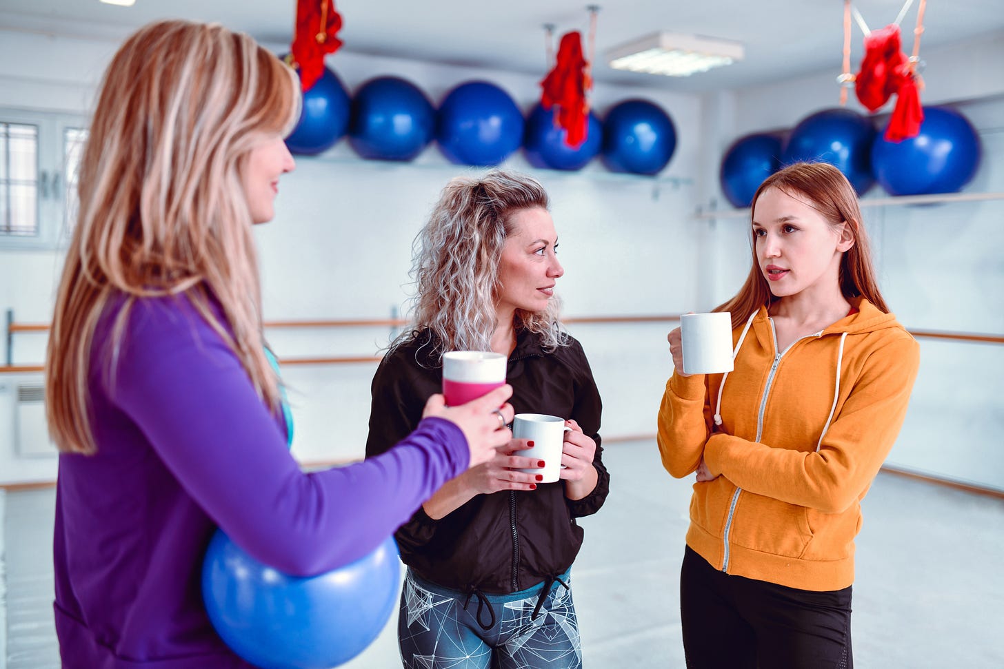 Three women talking in a fitness room holding cups of coffee. Three women talking in a fitness room holding cups of coffee.