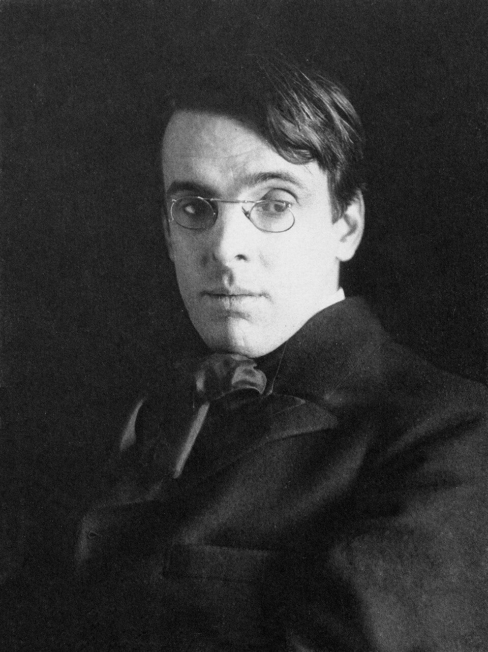 Black and white photo of Yeats in his 30s; wearing dark shirt with a frilly bow thing at neck; glasses, head turned three quarter, hair arranged loosely. Looks very poet-y Black and white photo of Yeats in his 30s; wearing dark shirt with a frilly bow thing at neck; glasses, head turned three quarter, hair arranged loosely. Looks very poet-y