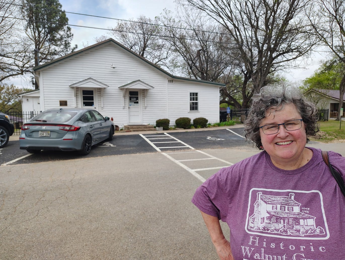 Annette in front of small whitewashed building and parking lot