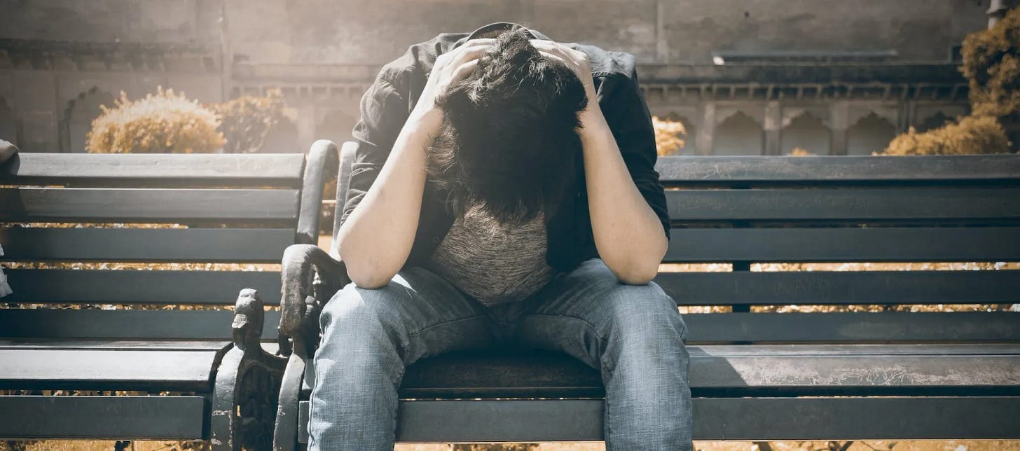 man in black shirt and gray denim pants sitting on gray padded bench