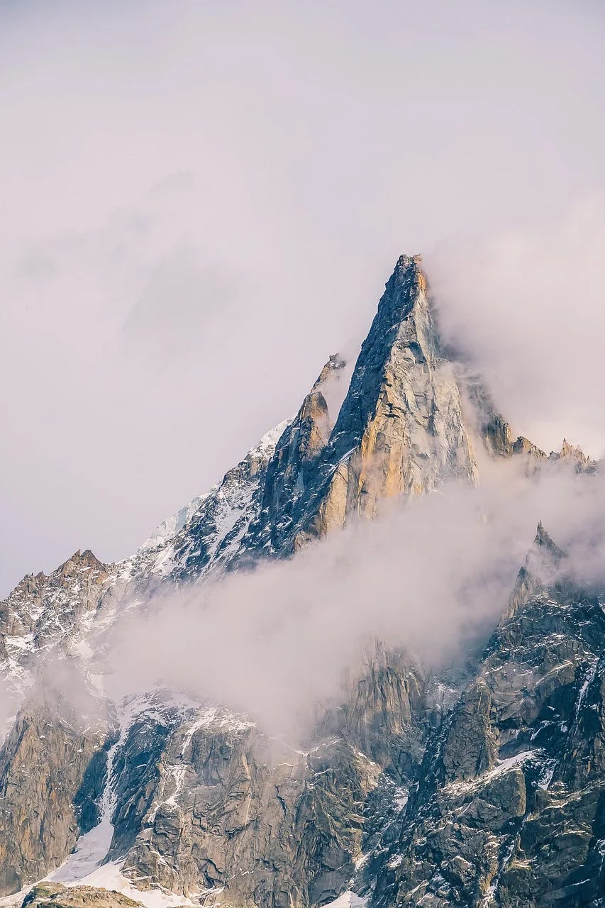 A photo of a distant mountain peak with clouds and fog near the summit