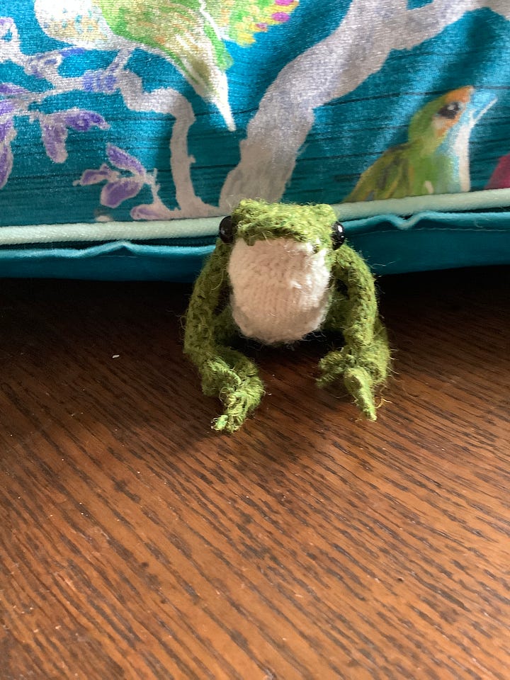 A tiny knitted frog in a cream jumper in a variety of poses, one without the jumpers and looking balletic