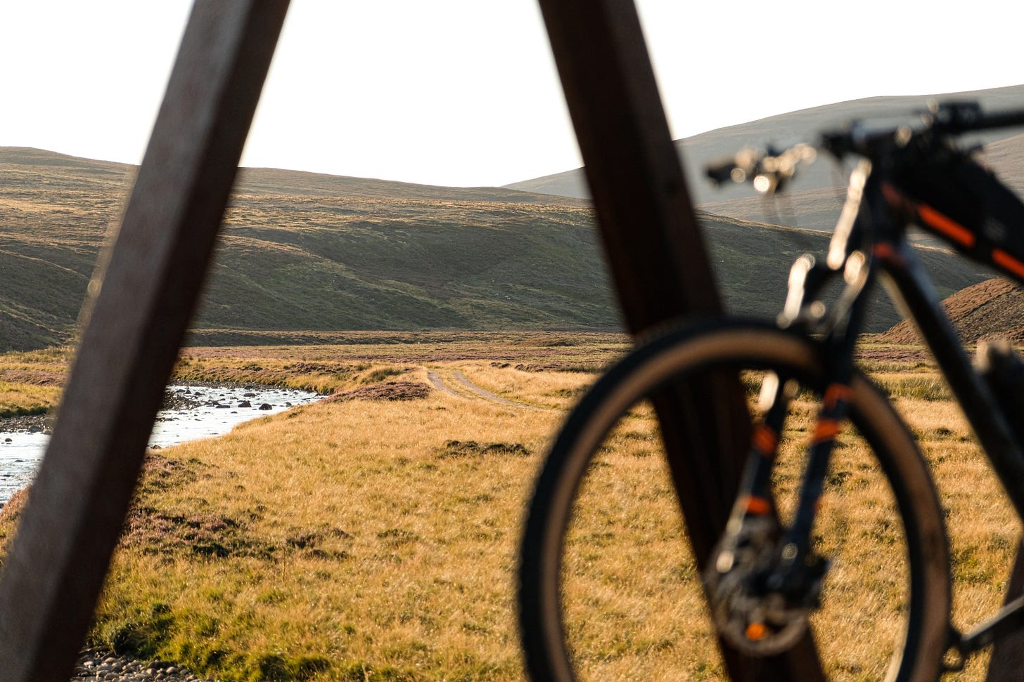 A bike leans against a small bridge in the foreground, out of focus. Beyond it, a long estate track stretches into the distance, glowing in the warm light of sunset.