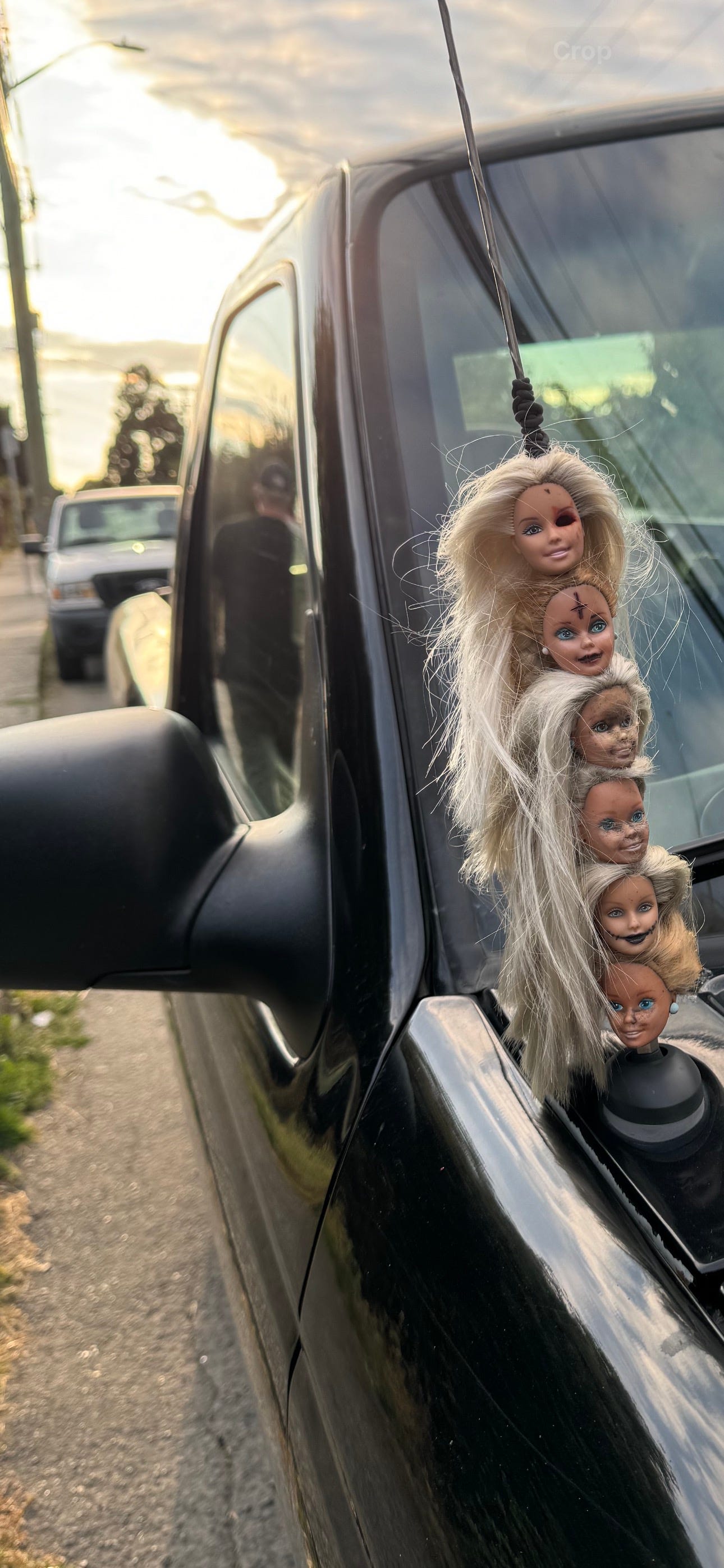 Six severed Barbie heads stuck on the antennae of a black truck.