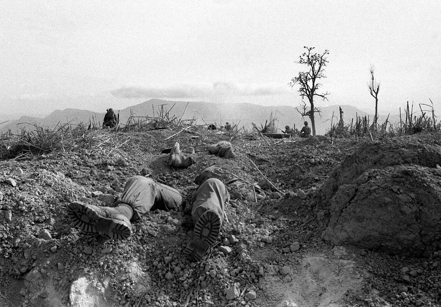 April 1968, Hill 689, Khe Sanh: A grim scene where fallen U.S. Marines lie half-buried, with comrades standing guard after a brutal battle against entrenched North Vietnamese forces. April 1968, Hill 689, Khe Sanh: A grim scene where fallen U.S. Marines lie half-buried, with comrades standing guard after a brutal battle against entrenched North Vietnamese forces.
