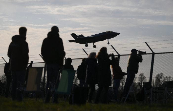 Spectators watch an F-35 fighter jet landing.
