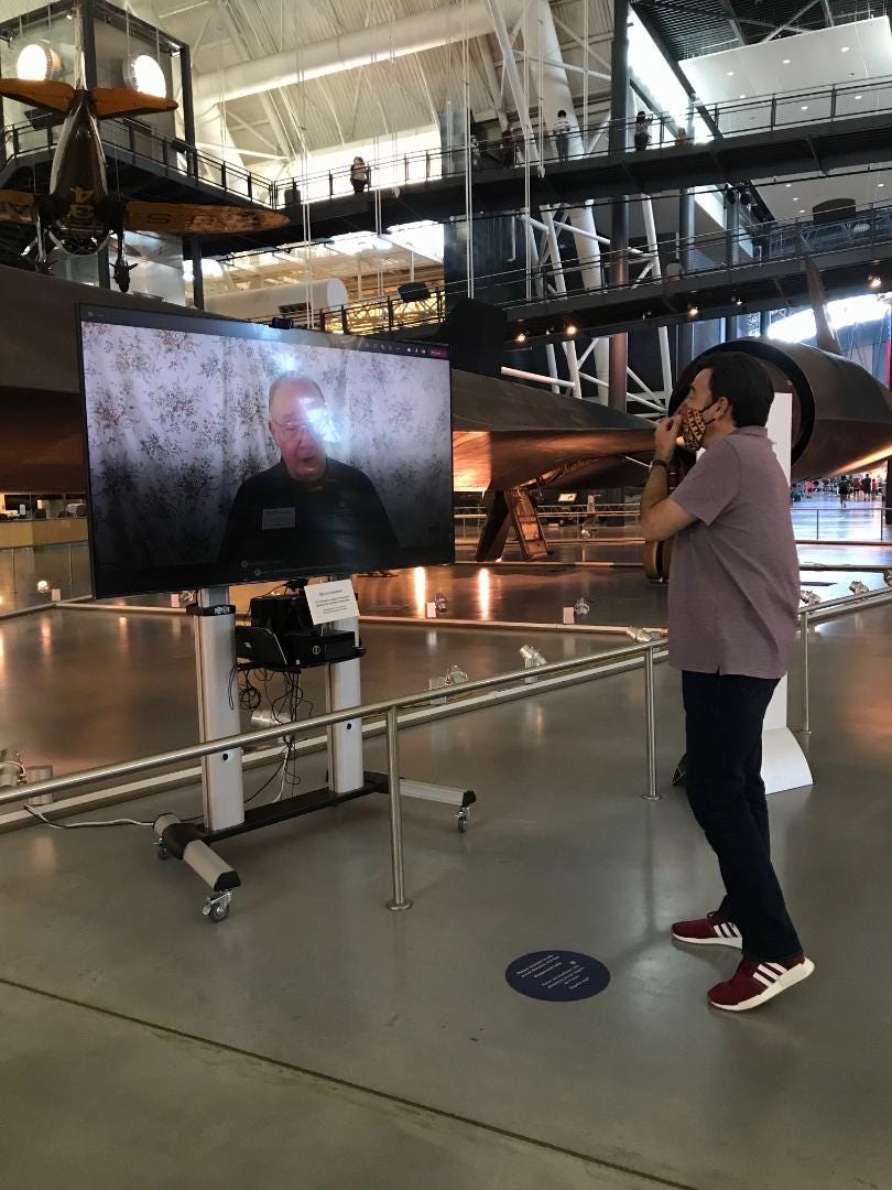 Docent on a television screen talking to me in person in front of an SR-71 Blackbird aircraft. Docent on a television screen talking to me in person in front of an SR-71 Blackbird aircraft.