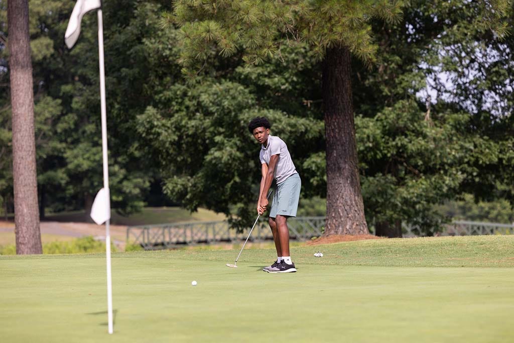 Young man in a grey polo lining up a putt on a golf green near a white flag. Young man in a grey polo lining up a putt on a golf green near a white flag.