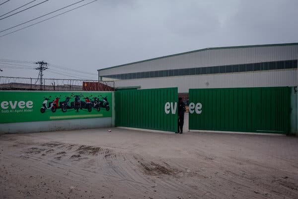 A person swings shut a large, green industrial gate painted with an Evee logo.