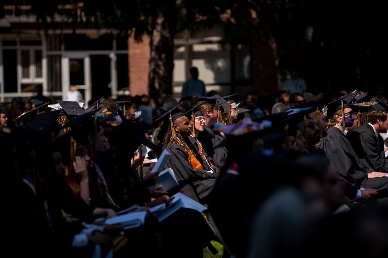 Graduates sit outside on a sunny day during commencement ceremonies