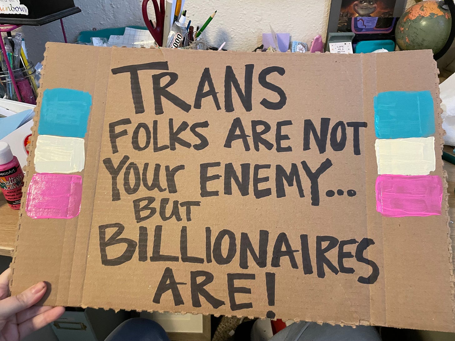 a cardboard sign says trans folks are not your enemy but billionaires are