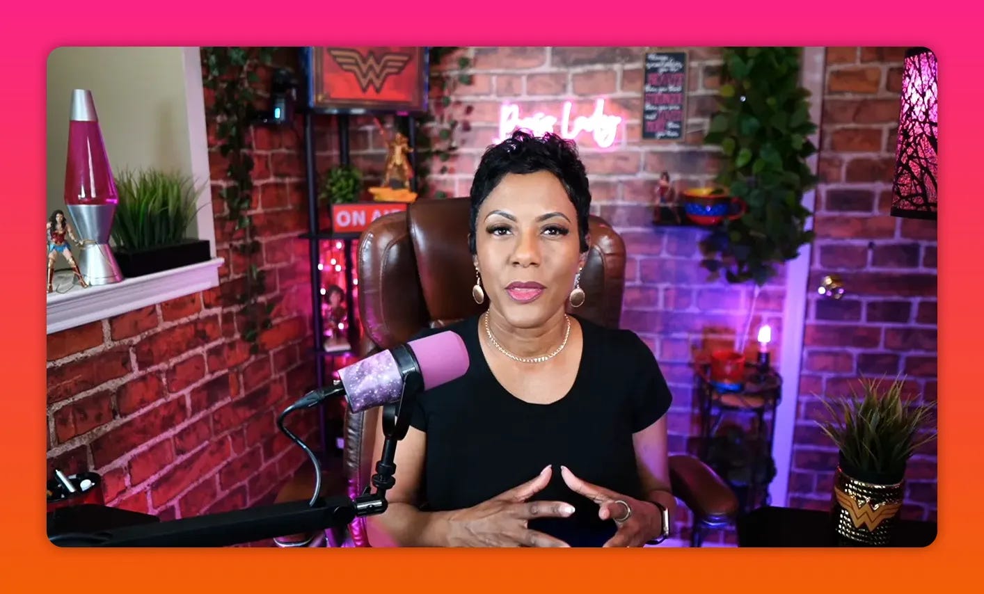 Host looking directly into camera with a confident, neutral expression in a brick-walled home studio and a visible pink microphone.