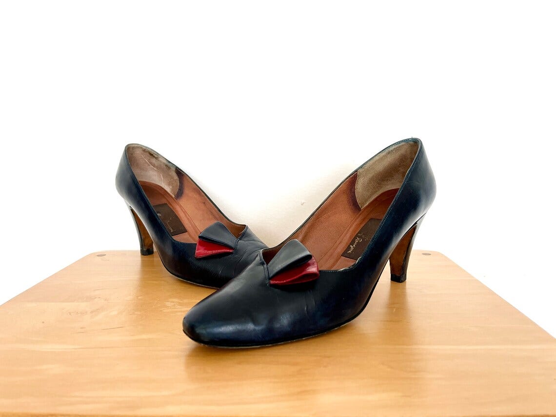 May include: A pair of navy blue leather heeled shoes with a red and blue bow accent on the front of each shoe.