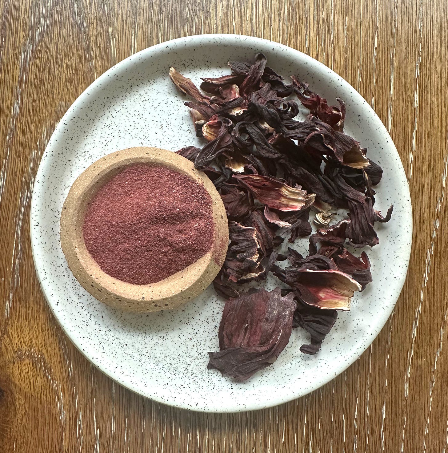 overhead image of hibiscus powder on plate next to dried hibiscus petals