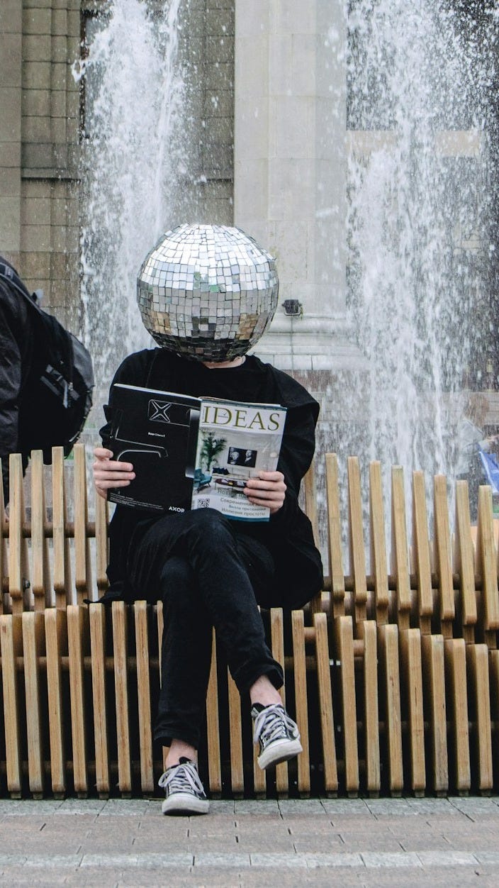 person sitting on wooden accordion bench while reading magazine at the back of water fountain