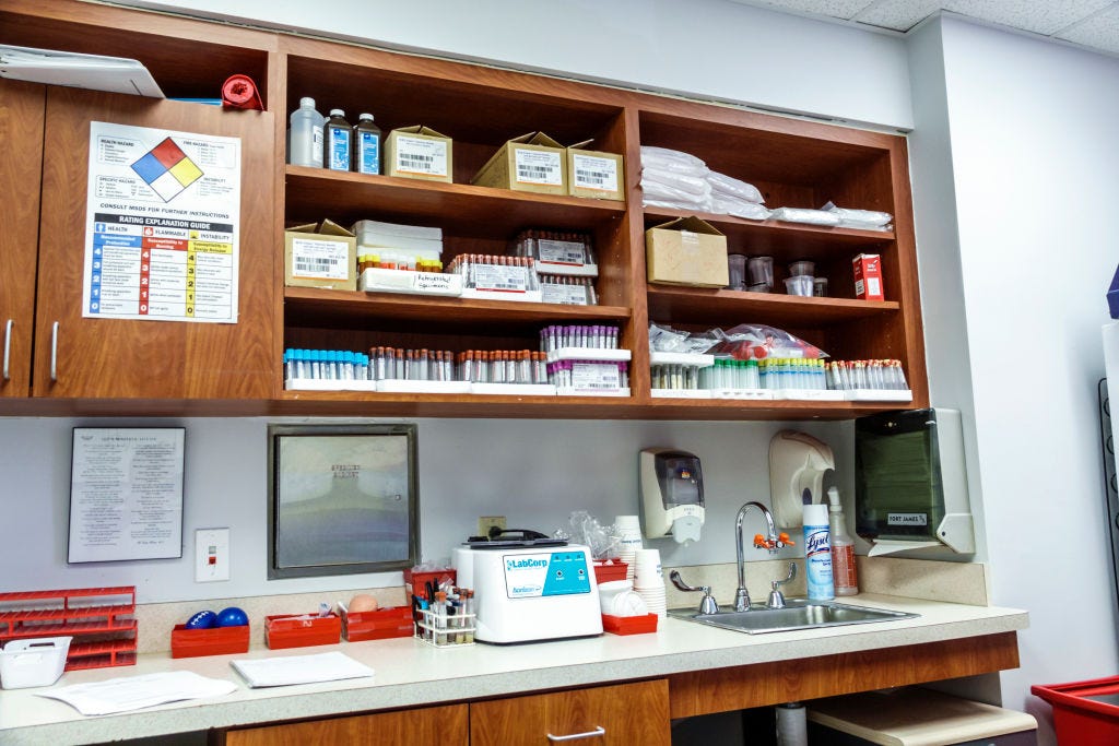 Rows of test tubes and other medical supplies sit on wooden shelves above a work bench in a doctor's office